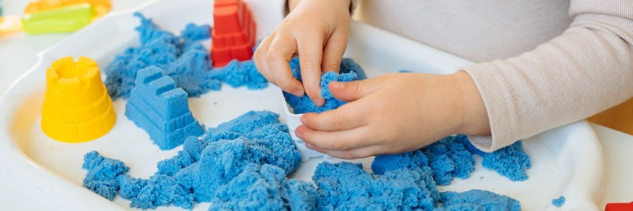Dłonie dziecka bawiącego się niebieskim piaskiem kinetycznym.