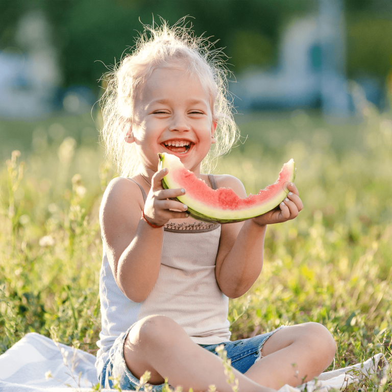 Radosne małe dziecko je zdrowy podwieczorek na trawie w słoneczny dzień.