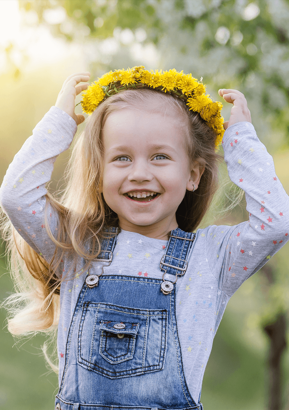 Radosna przedszkolna dziewczynka zakłada na głowę kolorowy wianek z kwiatów.