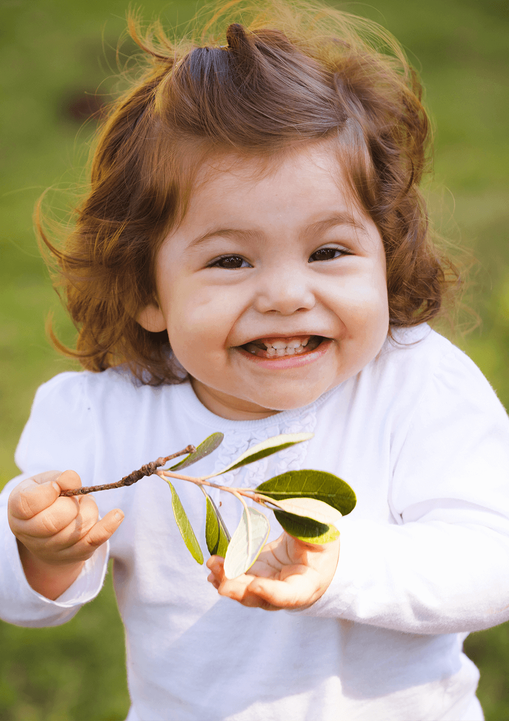 Radosne małe dziecko z żłobka trzyma w dłoni liść i uśmiecha się.