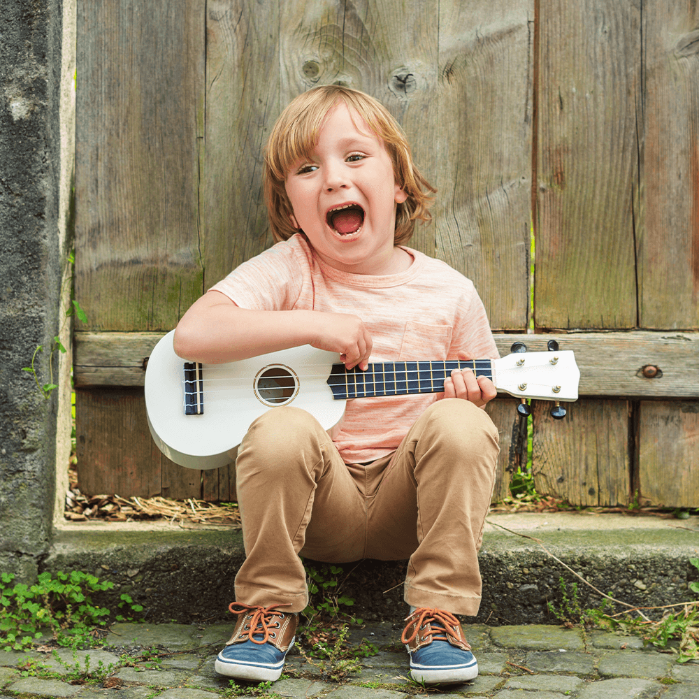 Wizerunek dziecka grającego na gitarze i śpiewającego podczas zajęć z rytmiki.