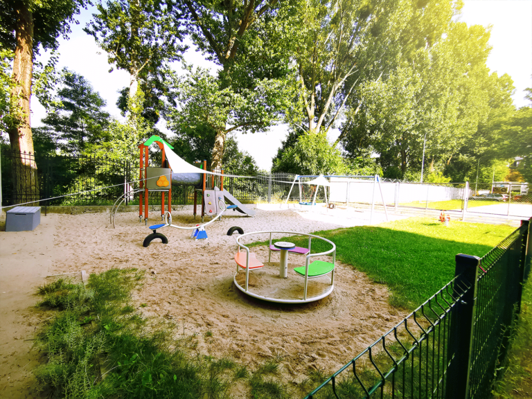 Widok na kolorową karuzelę i urokliwy małpi gaj na podwórku przedszkolnym.