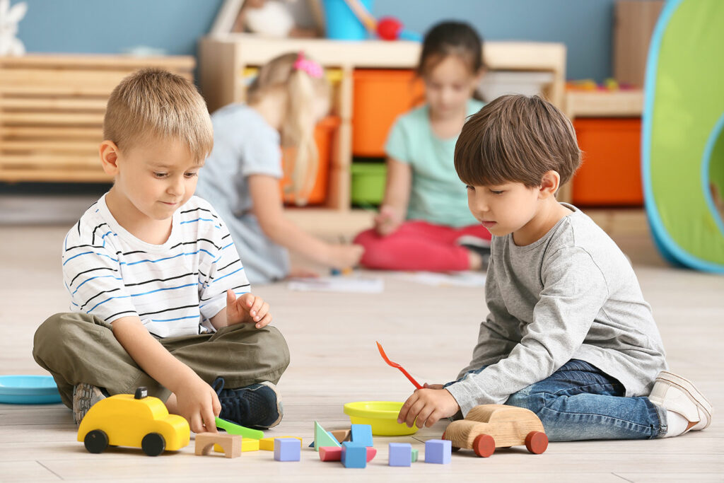 Dwójka uśmiechniętych przedszkolaków bawiących się kolorowymi zabawkami.