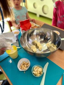 Nauczycielka i dzieci przygotowują składniki jabłkowego ciasta podczas wspólnych zajęć w przedszkolu.