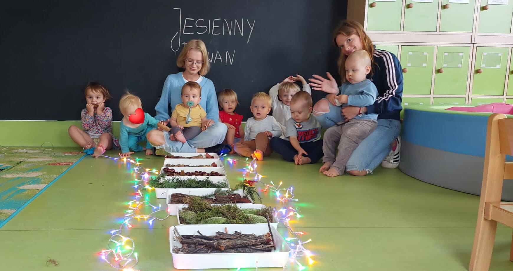 Grupa uśmiechniętych maluchów wesoło pozuje przy kolorowej, jesiennej ścieżce sensorycznej.