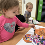 Dziewczynka maluje misia brązową farbą na kartce papieru.