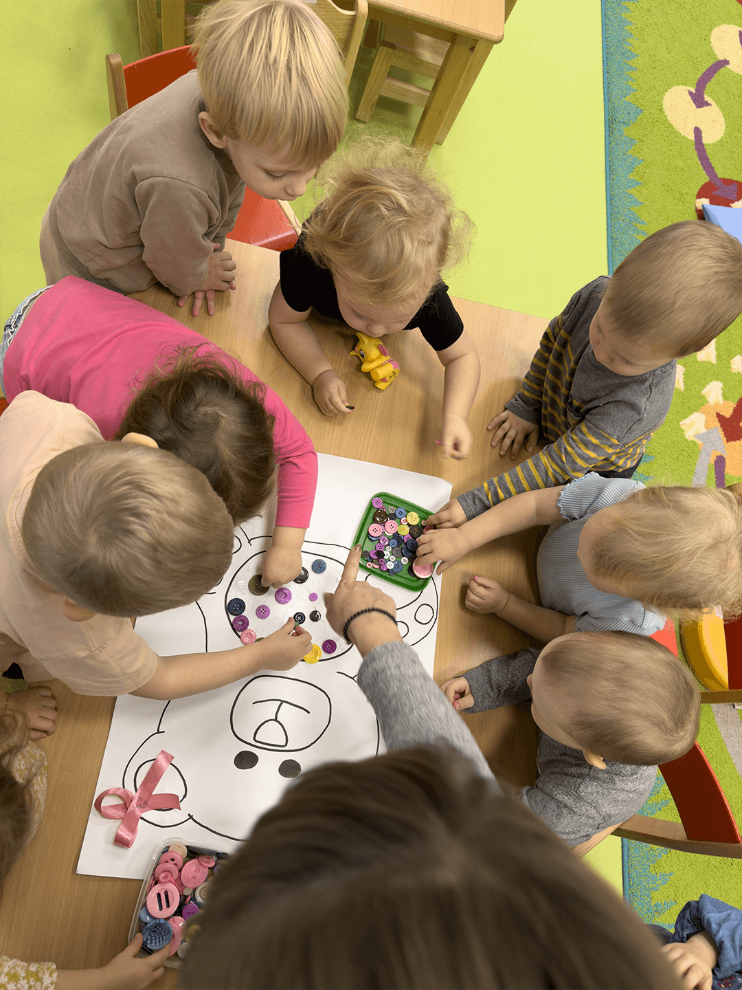 Uśmiechnięte dzieci w żłobku tworzą wspólnie misia podczas kreatywnej zabawy plastycznej.