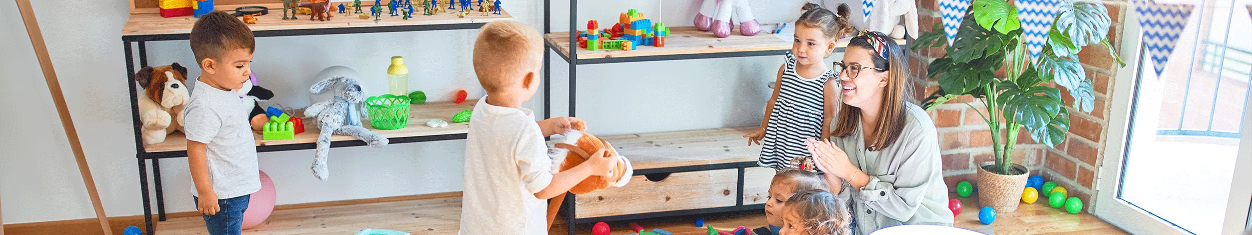 Opiekunka bawi się z dziećmi w przedszkolu w dużej sali z zabawkami